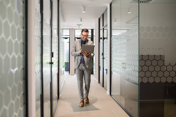 istock Full length of male software developer researching online over laptop while walking in office corridor 2169448355