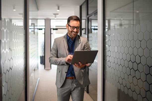 Portrait of developer smiling and doing online research over laptop while walking in office corridor