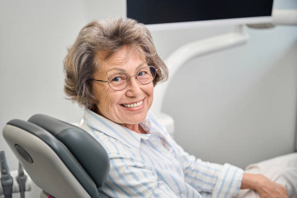 Gray-haired elderly woman sits in a dentists chair stock photo