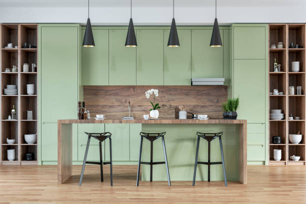 istock A front view of a modern pastel green, white and hardwood kitchen with rectangular breakfast kitchen island with stools, pendant lights 2169452172