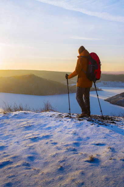Man hiker hiking using backpack and trekking poles in winter nature.