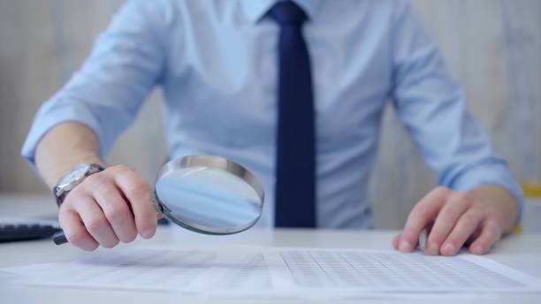 istock Businessman is carefully examining financial documents with a magnifying glass, highlighting the importance of thorough analysis in business. Audit and taxes 2169460968