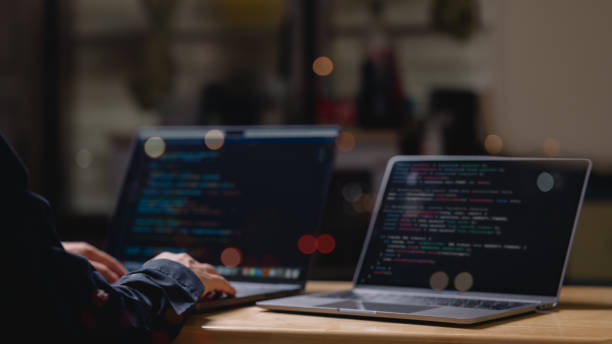 A person is typing coding on a laptop computer with a black screen. The laptop is open to a webpage with a lot of code. The person is focused on the task at hand