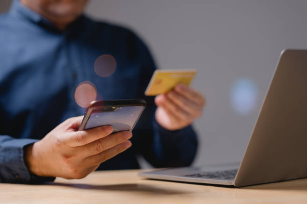 istock Transactions convenience and modern technology concept. A man is using his phone and laptop to pay for something. He is holding a credit card in one hand and a phone in the other. 2169466136