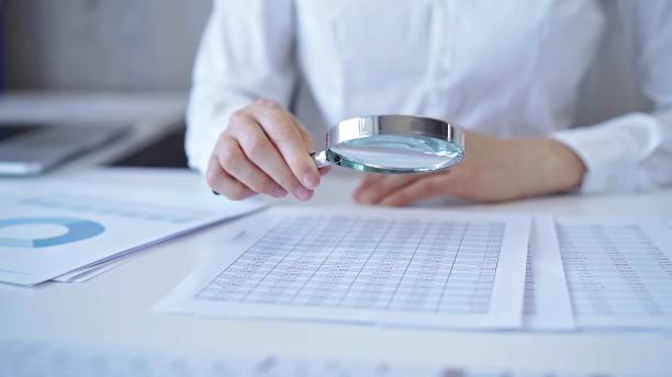 istock Businesswoman with white blues is analyzing financial data on a spreadsheet using a magnifying glass. Audit and taxes 2169467425