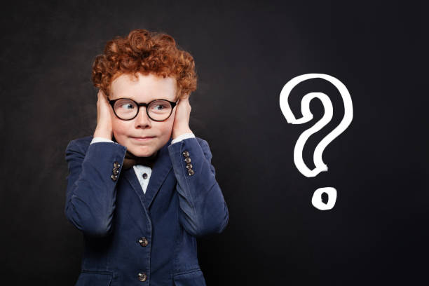 istock Unsure child boy school student covers his ears with his hands against blackboard background with question mark. Idea and Education concept 2169481052