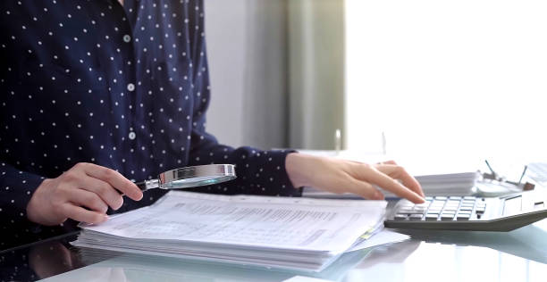 istock A businesswoman is using a calculator and a magnifying glass to analyze financial documents at her desk in a modern and fair office setting, focusing on aspects of audit and taxes in business 2169486638