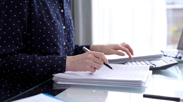 istock Businesswoman making notes while reviewing ring folder of financial documents with magnifying glass at desk in modern office. Audit and taxes in business 2169487059