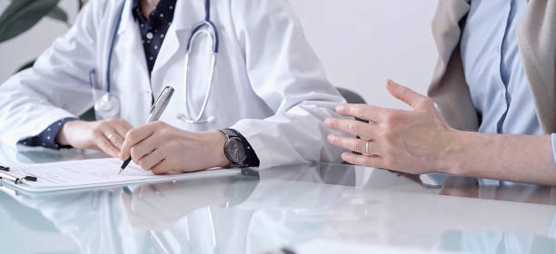 istock Doctor consulting patient in clinic. Female physician is writing notes while talking with a man, close up. Medicine concept 2169489087