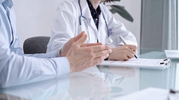 istock Doctor consulting patient in clinic. Female physician is writing notes while talking with a man wearing blue shirt, close up. Medicine concept 2169489906