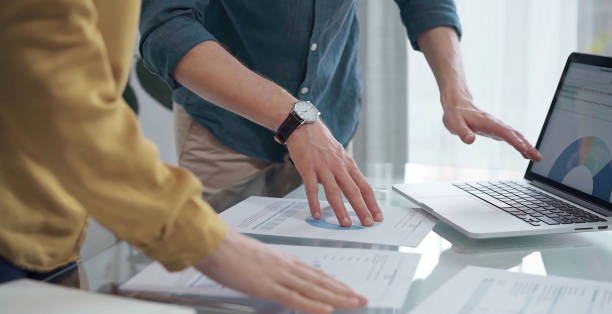 istock Business people, professionals analyzing financial charts and data on a desk while standing and using laptop computer in office 2169491584