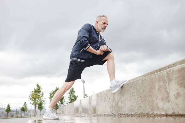 istock Mature Man Lunging Stretching Leg Muscles against Overcasted Sky in Park 2169495130