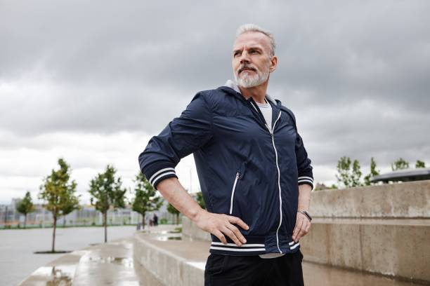 Mature Man Resting after Jogging in Park against Cloudy Sky