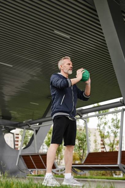 istock Elderly Man Standing with Ball Doing Squat Exercise at Park 2169495185