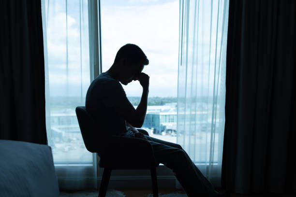 istock Depressed man sitting in room covering face with hands in despair. 2169498367