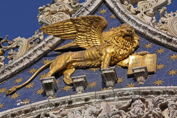The bronze winged lion statue on St Mark’s Square is the iconic symbol of Venice with the ornate façade of St Mark’s Basilica blurred in the background