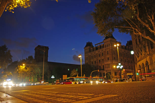 Nighttime cityscape with long exposure capturing blurred traffic lights, illuminated street lamps, buildings, silhouetted against a dark blue sky and close-up of pavement.