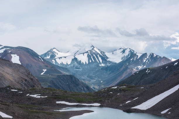 istock Dramatic view to most beautiful blue alpine lake against snow-covered range with few pointy peaks. Atmospheric landscape with azure mountain lake against three snowy peaked tops under gray cloudy sky. 2169519210
