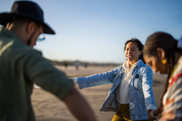 A cheerful gathering of friends, of various ethnic backgrounds, enjoy dancing on a sunlit beach, their casual attire and joyful poses reflecting a relaxed, leisurely day by the sea.