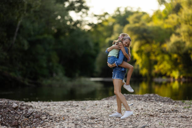 Full length shot of mother carrying and hugging her lovely daughter by the river