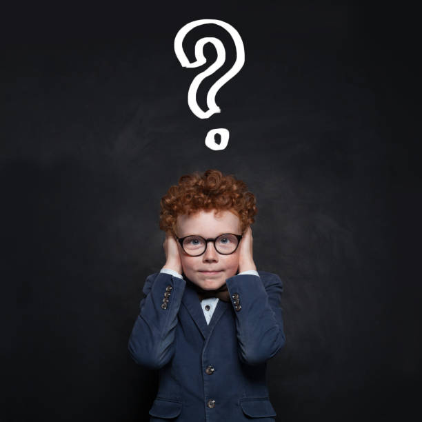 istock Young school student boy covering his ears with his hands and looking at camera against blackboard background with question mark. Idea and Education concept 2169541388