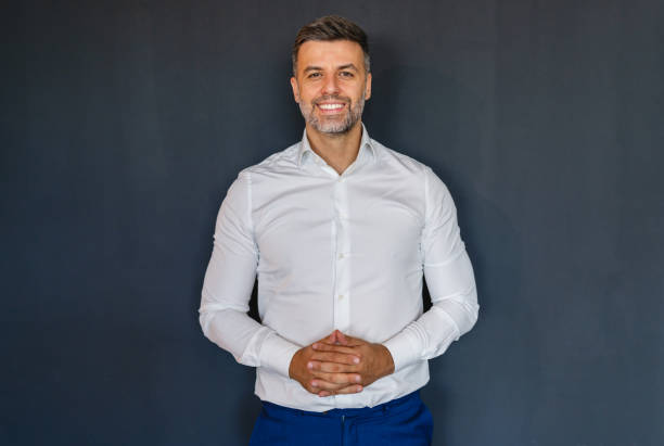 Smiling man posing in white shirt against dark background