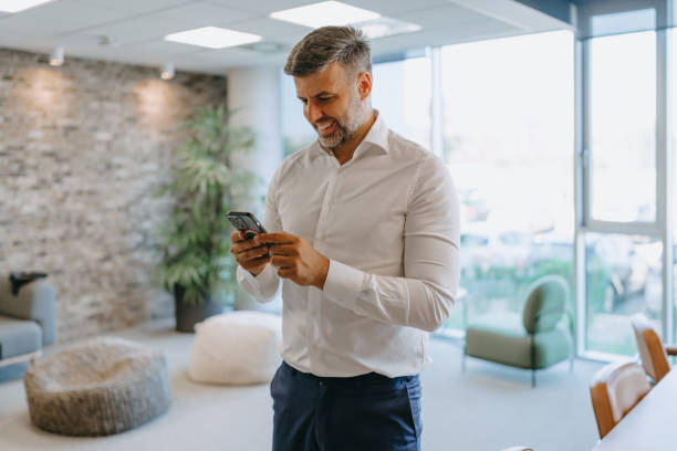 istock Man standing using smartphone in well-lit modern office 2169550822