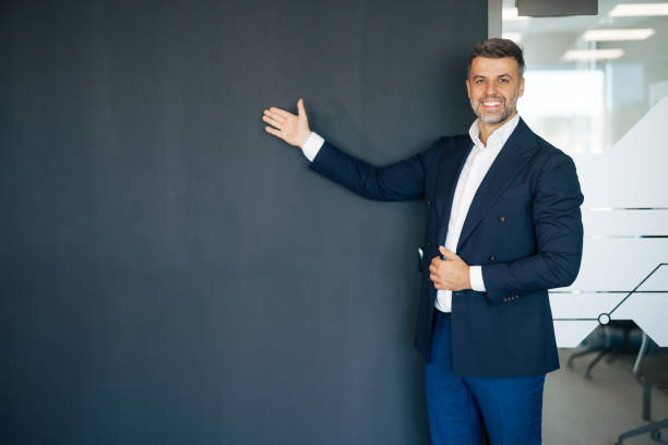 istock Man pointing to blank wall in formal business attire 2169551365