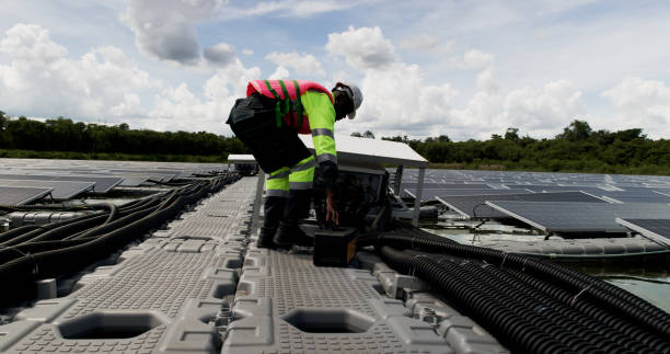 An African-American engineer carefully examines a cutting-edge floating solar panel system designed to harness renewable energy for an industrial complex. Leveraging their specialized skills, the engineer meticulously inspects and oversees the installation process to ensure it aligns with the project's blueprints and specifications.