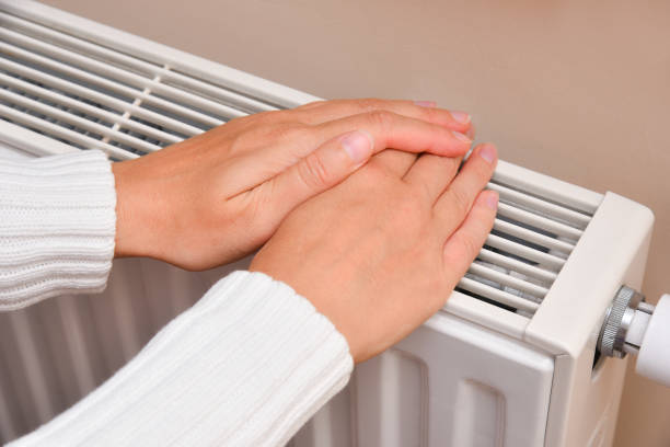 istock Woman warms her hands over a radiator at home 2169558082