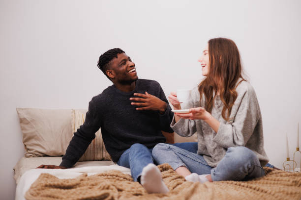 istock Cheerful multiethnic couple with coffee talking on bed at home 2169558678