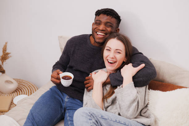 istock Smiling interracial couple with coffee looking at camera while relaxing on bed at home 2169558692