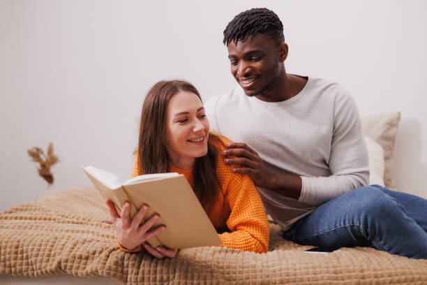istock Smiling african american man hugging girlfriend reading book at home 2169558729