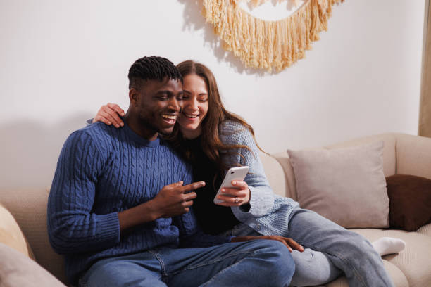 istock Cheerful multiethnic couple using smartphone on couch at home 2169558848