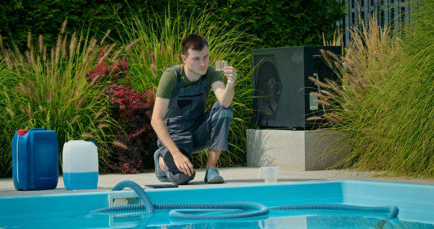 istock Pool maintenance technician analyzing water sample beside a swimming pool surrounded by greenery and chemical containers. 2169563889