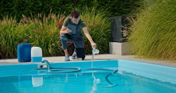 istock Pool technician pouring liquid into the pool while using a tablet, with chemical containers and greenery in the background. 2169563958