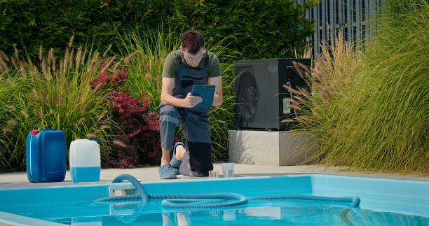 istock Pool technician checking data on a tablet beside a swimming pool with chemical containers and lush greenery. 2169564030