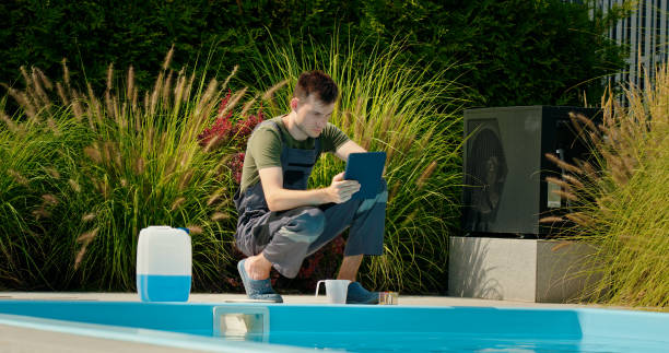 istock Pool technician using a tablet by the pool, surrounded by greenery and a chemical container, focused on maintenance tasks. 2169564741