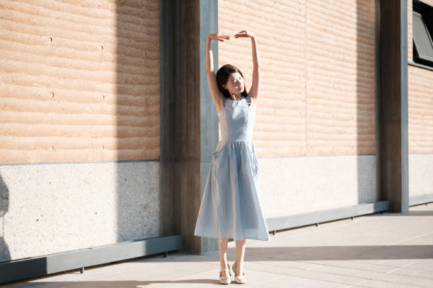 A woman dances beside a building wall