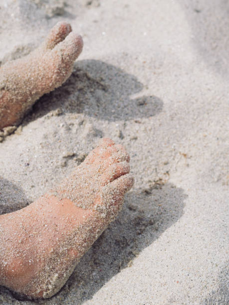 This vertical close-up captures the innocent charm of a toddler’s feet covered with the soft, white sand at the Sardinian seaside. The delicate toes in the serene beach setting. The warmth of the sand and the tranquil seaside atmosphere evoke the simple joy of a child’s first steps by the shore, creating a timeless moment of connection with nature. The shot highlights the softness of the feet against the natural texture of the sand, embodying the essence of a carefree day at the beach.