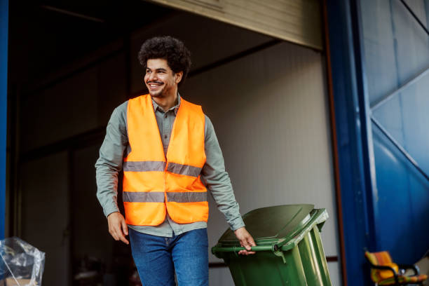 Smiling multicultural warehouse worker taking out trash. Diverse storage manual worker with trashcan taking out garbage. garbage stock pictures, royalty-free photos & images