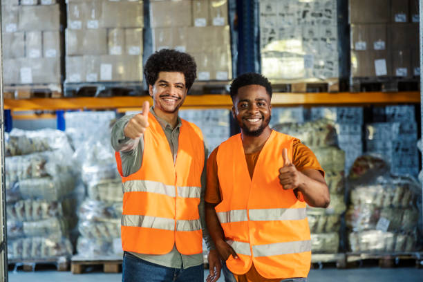 istock Interracial warehouse manager and worker standing at facility and giving thumbs up while smiling at camera. 2169584754