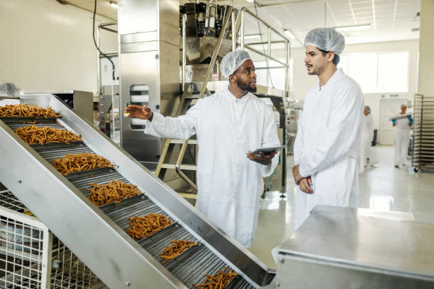 istock Multicultural supervisor in sterile uniform holding tablet and checking on production line while talking to operator 2169584789