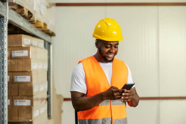 istock Diverse warehouse worker standing at facility with cellphone in hands and smiling at it while tracking shipment online. 2169585327