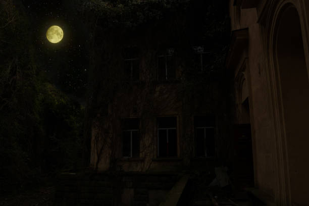 Dark landscape with yellow full moon in the night sky shining above the silhouette of an abandoned building