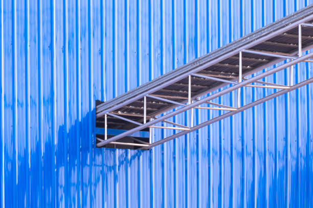 Overhead electrical cable ladder tray for installing power and control cable lines from the outside into blue aluminum corrugated metal wall of industrial building