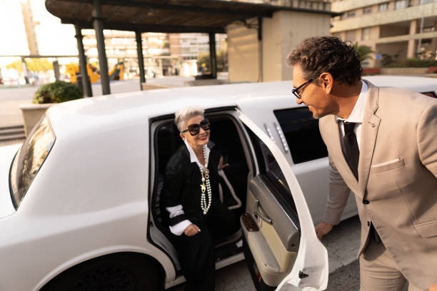 Elegant senior businesswoman exiting limousine with chauffeur Elegant senior businesswoman is exiting a limousine with the help of her chauffeur in the city celebrity limo stock pictures, royalty-free photos & images