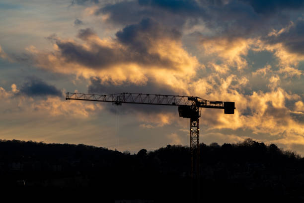 Tall cranes and cargo containers by light poles at commercial dock in front of orange sky during sunset
