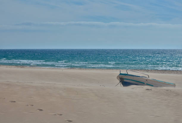 Boat, white sand, blue sea and sky in the dunes of Bolonia beach, Cádiz