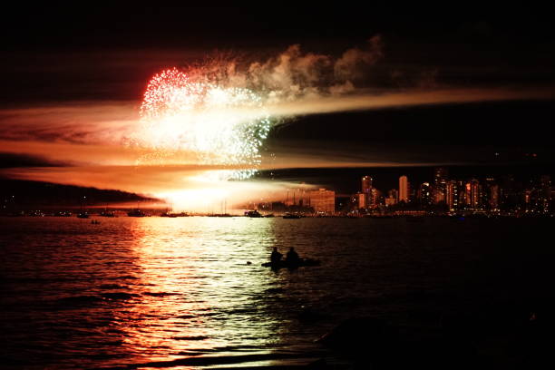 Captured on July 20, 2024, this photograph showcases a breathtaking fireworks display over Vancouver's harbor. The vibrant bursts of color light up the sky, reflecting beautifully off the water. In the foreground, silhouettes of kayakers add a sense of scale and adventure, perfectly complementing the festive atmosphere. The city skyline twinkles in the distance, providing a stunning backdrop to this quintessential Vancouver summer evening.